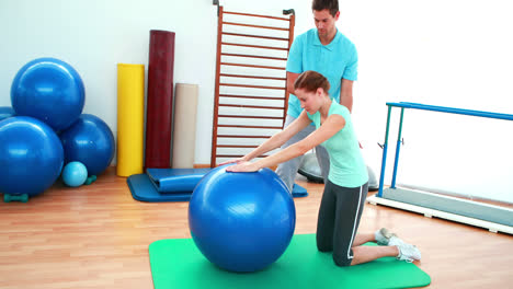 trainer helping his client stretch her back with exercise ball