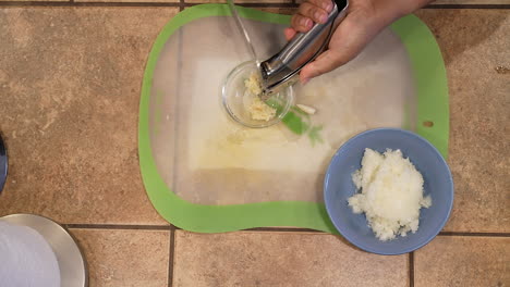 mincing organic garlic in a press for use in a homemade vegan recipe - overhead view wild rice series