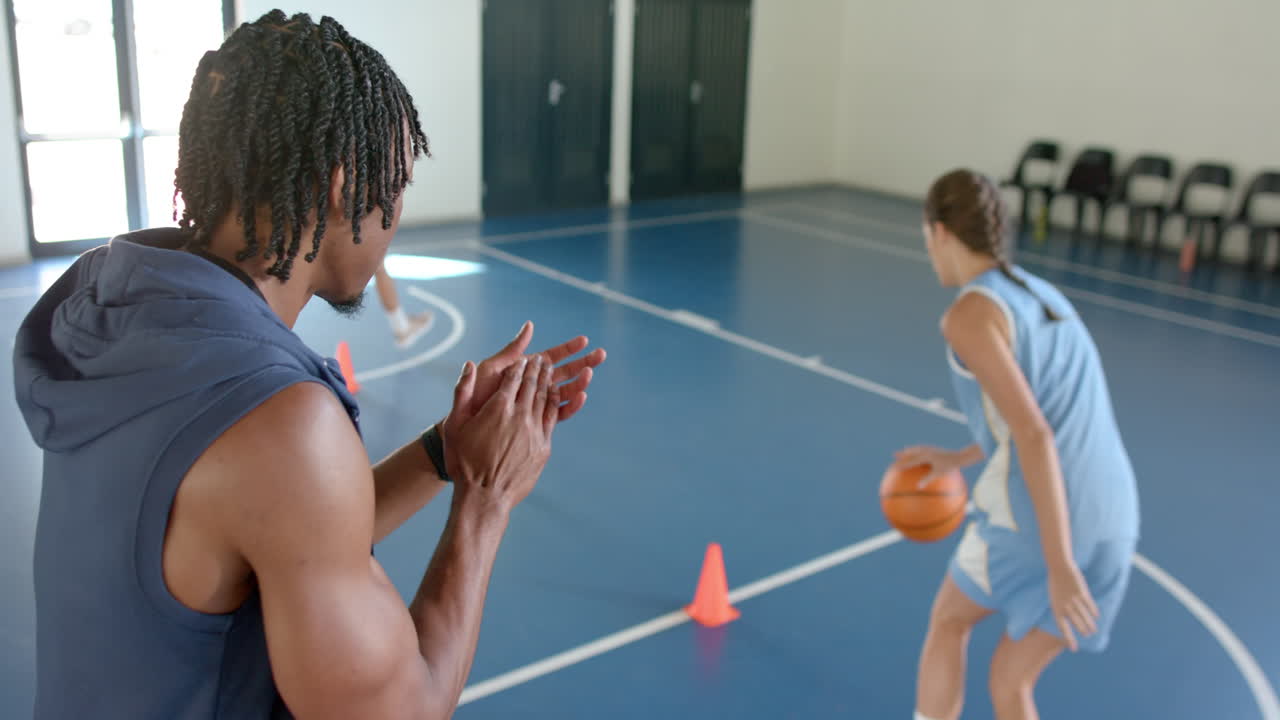 Coaching basketball practice, trainer clapping while female players dribbling in gym