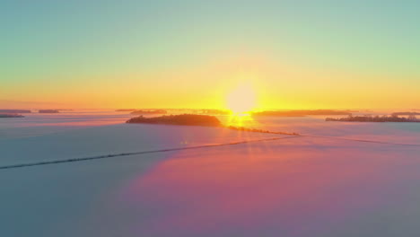 aerial drone flying over snow covered landscape with snow covered farmland at sunrise along bright yellow sky