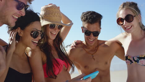 Mixed-race-group-of-friends-taking-selfies-on-the-beach-using-phone-camera