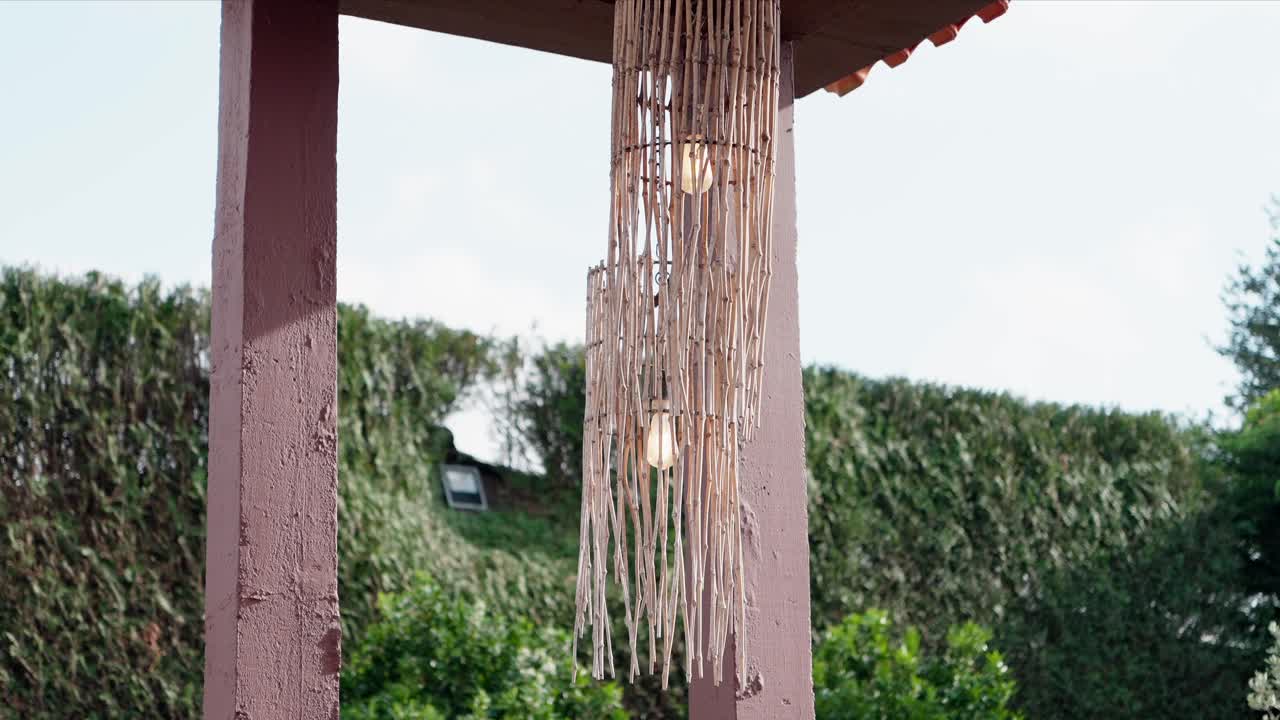 natural bamboo lamp fixture with exposed bulbs suspended on wooden outdoor frame