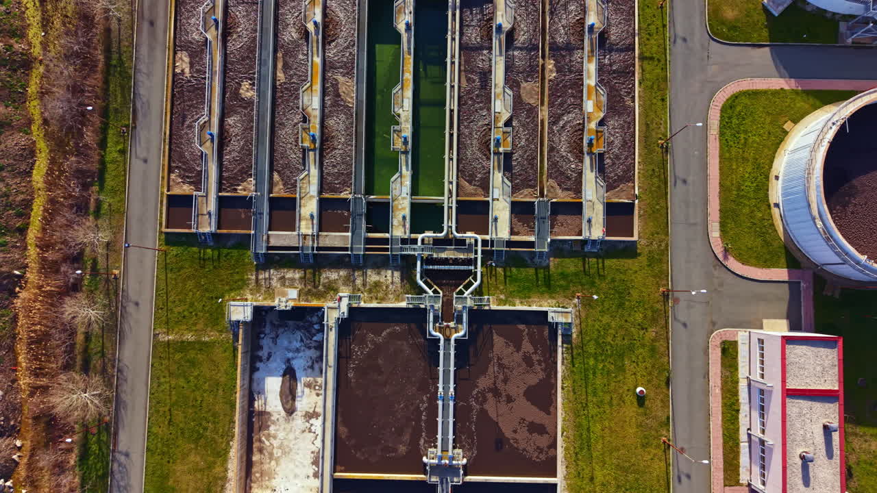 Un impianto di trattamento dell'acqua mostra numerosi grandi serbatoi e strutture sotto un cielo sereno durante il giorno con erba e sentieri nelle vicinanze.
