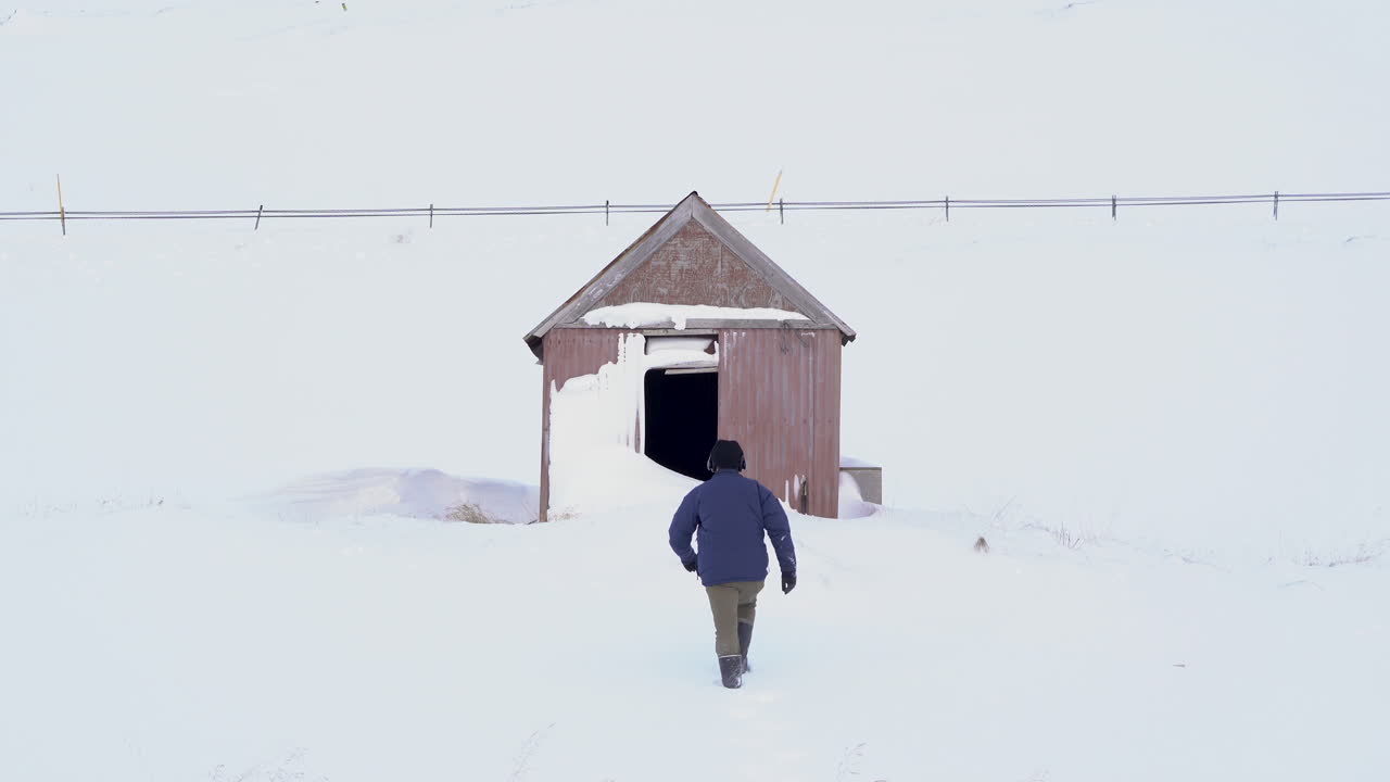 안정적인 샷, 눈 덮인 오두막을 향해 눈 속을 걷는 남자, 하얀 풍경