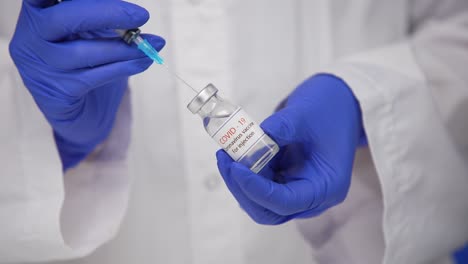 doctor with blue surgical gloves dials a coronavirus vaccine into a syringe to vaccinate against a worldwide epidemic sars-cov-2. blue screen, chroma key. close up. slow motion