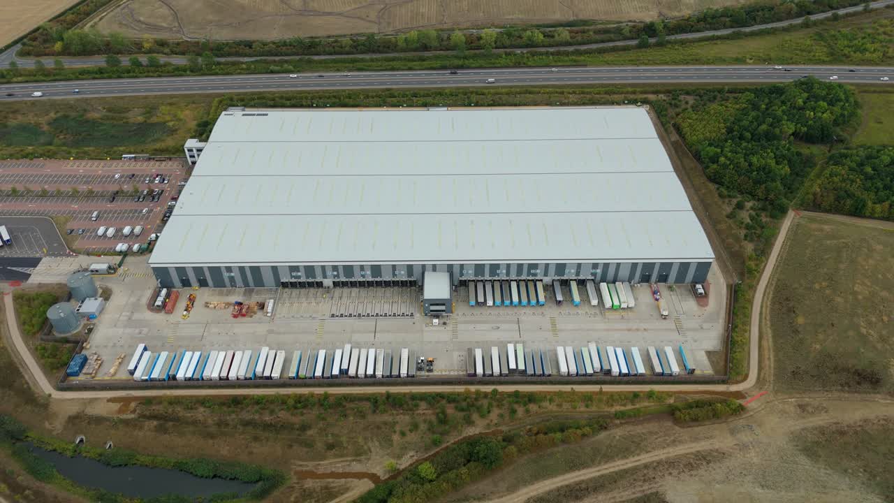 Vista aerea da drone di Bedford, Inghilterra, con traffico autostradale intenso e centri di distribuzione industriale, magazzini e fabbriche in un paesaggio commerciale