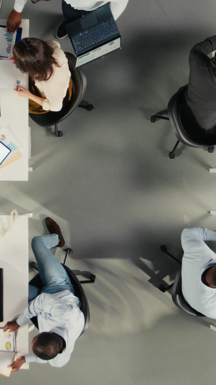 Vertical Video Top down view zoom out of corporate employees study business reports