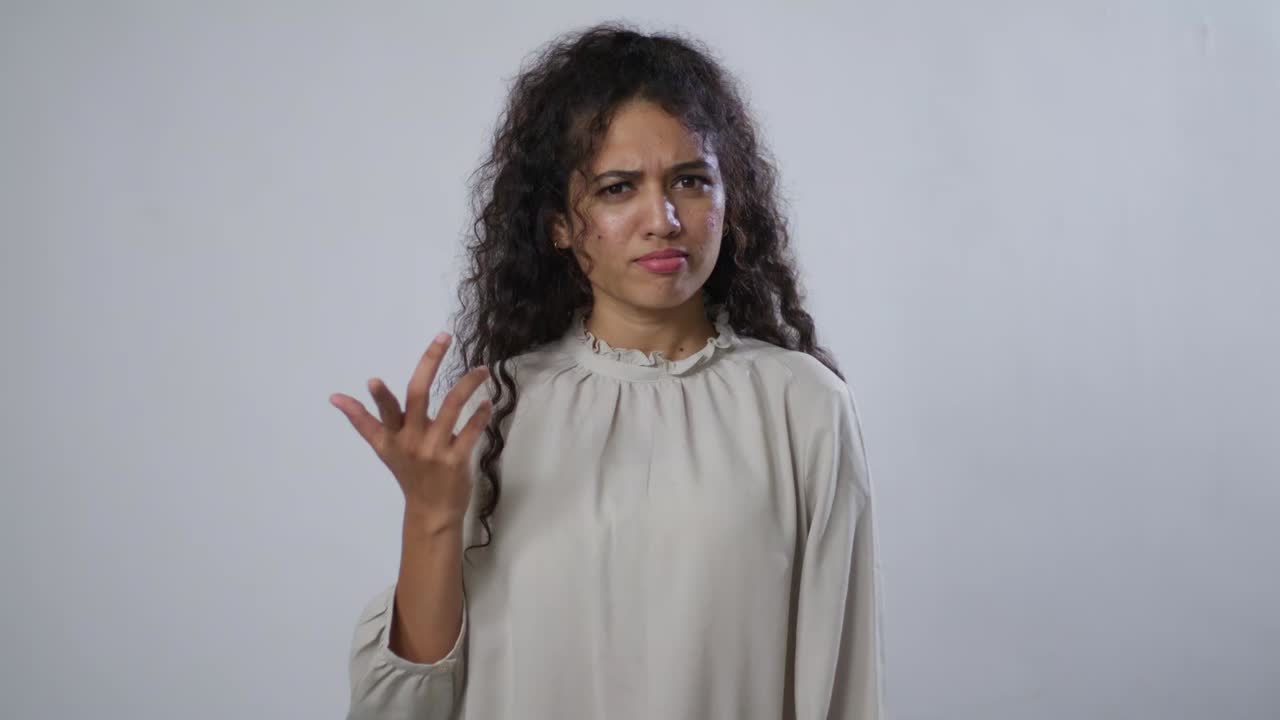 A South Asian woman with curly brown hair is gesturing with her hand, looking confused or annoyed