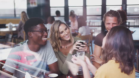 group of friends sitting at table in busy coffee shop talking