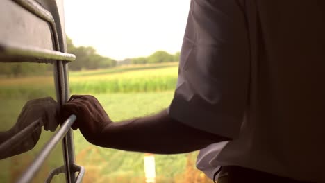 man holding railing on a train passing fields