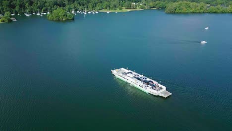 rotating aerial drone view of 500 year old car ferry on lake windermere from bowness nab to far sawrey with small boats moving through the scene on sunny summer morning showing algae in the lake