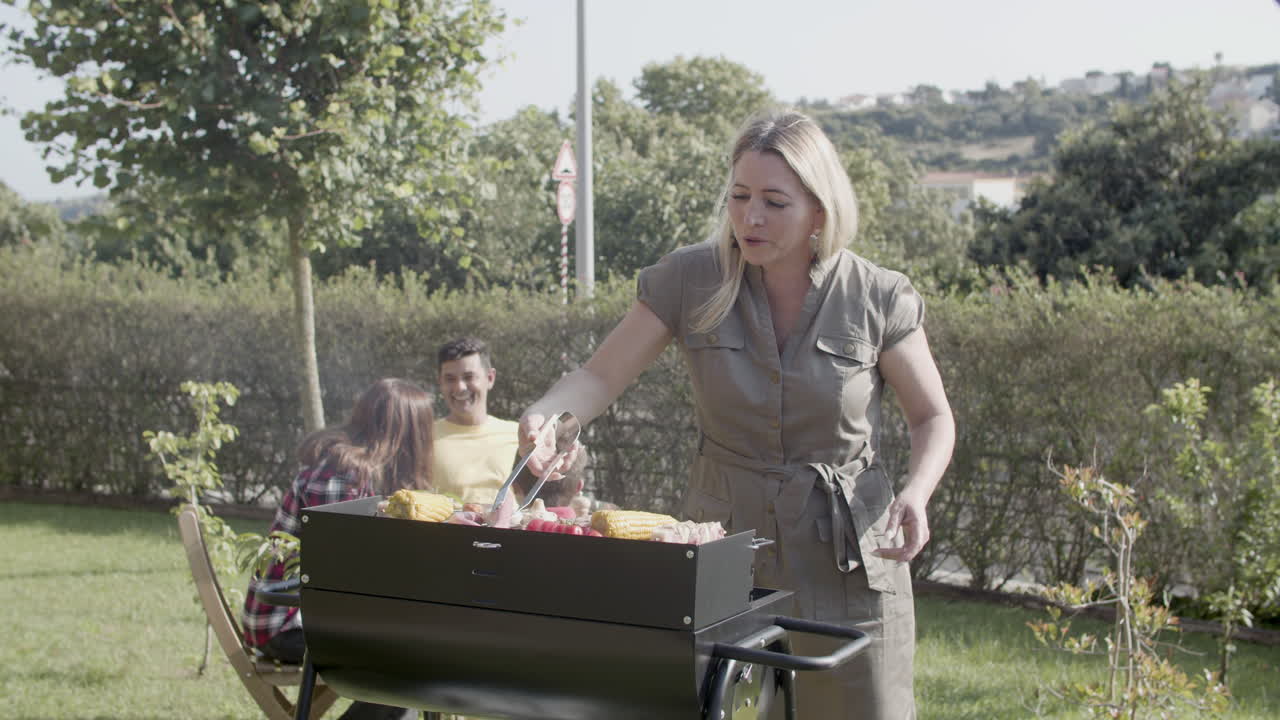 Mamma in piedi al barbecue che gira salsicce e funghi