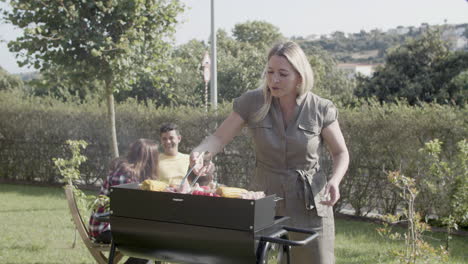 mum standing at grill and turning over sausage and mushroom