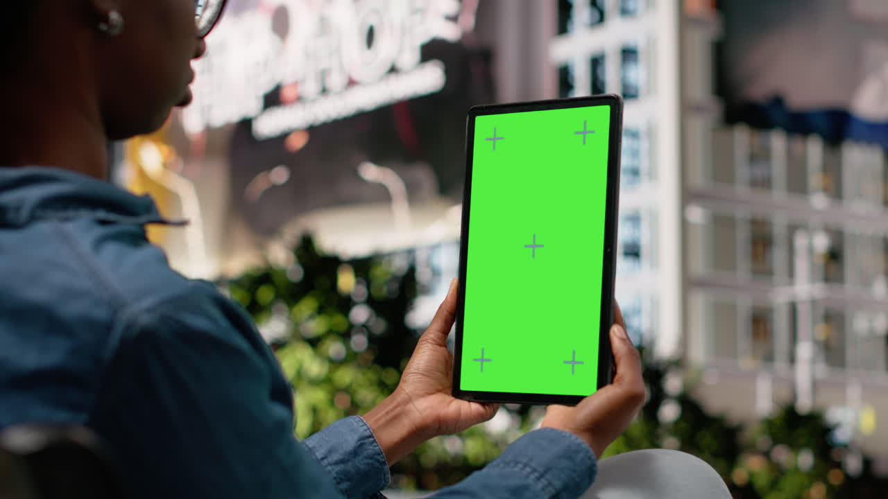 En person bruger en lodret tablet med grøn skærm til at se film, siddende på en bænk.