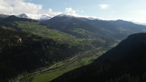 Aerial-view-overlooking-the-valley-of-Obersaxen,-Graubünden,-Switzerland,-surrounded-by-a-mountainous-range-with-snow-covered-peaks