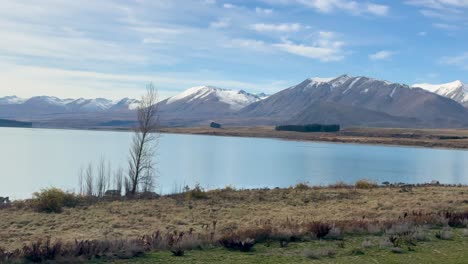 calm lake reflecting snow-capped mountains under a blue sky, captured in natural daylight with a tranquil atmosphere