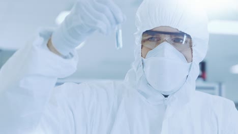 in the laboratory researcher / scientist wearing protective coverall holds test tube with experimental medicine and looks at it.