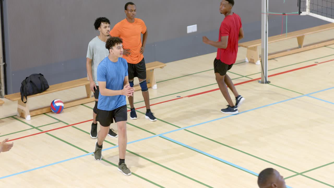 Após o lançamento da bola, colegas de equipe masculinos diversos defendendo, cortando e fazendo um levantamento por cima para um exercício sob a rede do ginásio.