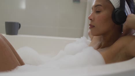 mixed race woman wearing headphones taking a bath and listening to music