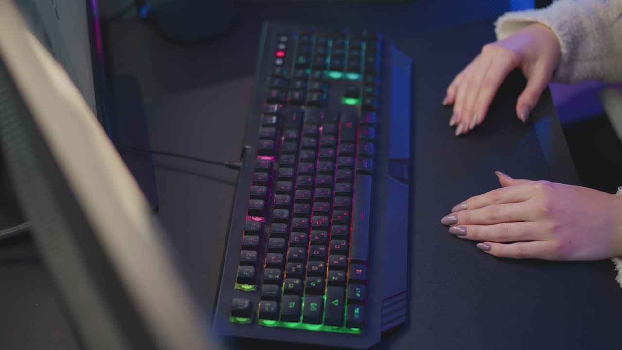 Aerial view of lady in fluffy sweater adjusting rgb keyboard near desktop screen glowing with vibrant colors in a modern workspace, fingers with polished nails interacting with mechanical keys