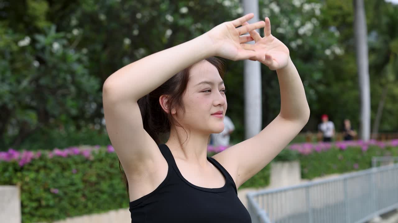黒のスポーツウェアを着た女性が、日中の公園の歩道でサイドストレッチをしている。