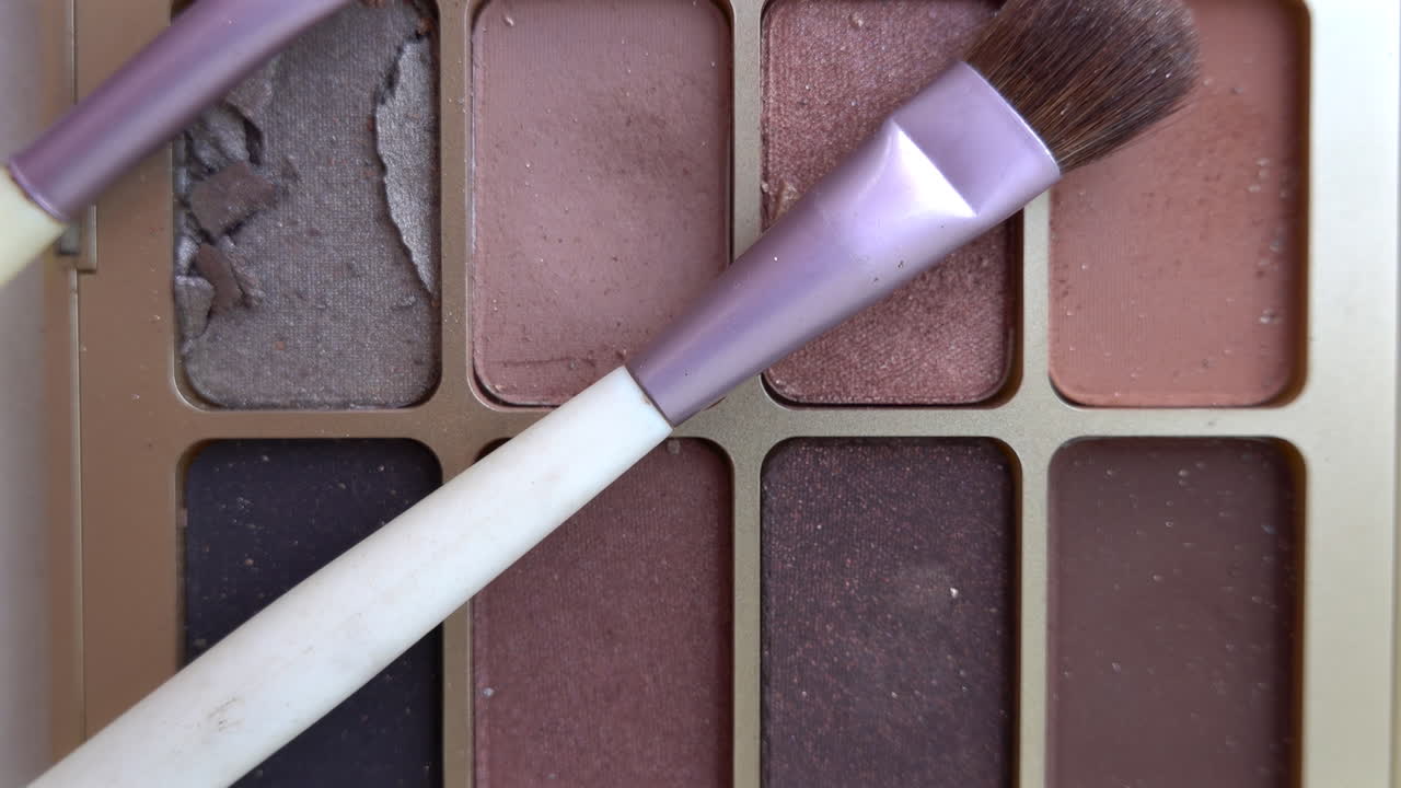 Close up of two purple make-up brushes on an eyeshadow palette