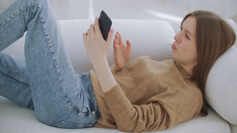Woman on a video call using a mobile phone. Mature woman with talking on smartphone while sitting at living room with modern interior. Concept of technology and relaxation.