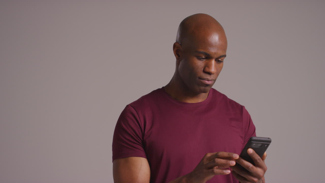 Studio Shot Of Mature Man With Mobile Phone Scrolling Online Checking Social Media And Messaging Against Grey Background