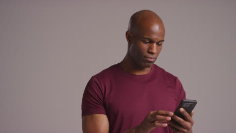 fotografía de estudio de un hombre maduro con teléfono móvil desplazándose por internet comprobando las redes sociales y los mensajes contra un fondo gris
