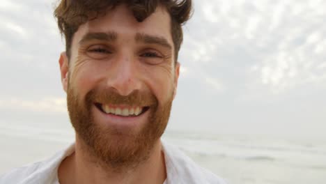 vista frontal de un joven feliz hombre caucásico sonriendo y mirando a la cámara en la playa 4k