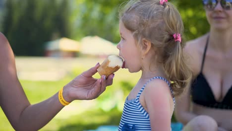 Close-up-Little-girl-child-in-bathing-suit-eats-ice-cream-which-woman-treats-her-on-beach