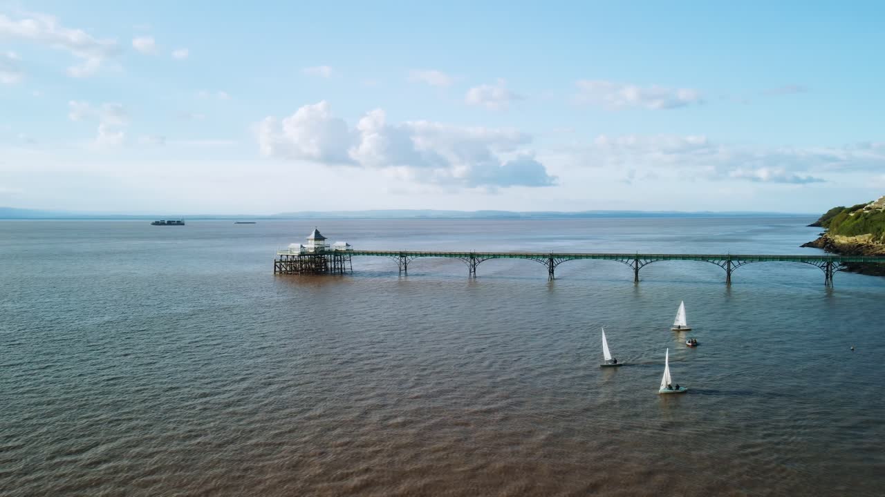 Et dronebillede med små sejlbåde i forgrunden og Clevedon Pier i baggrunden. Optagelsen drejer derefter 180 grader for at afsløre kysten