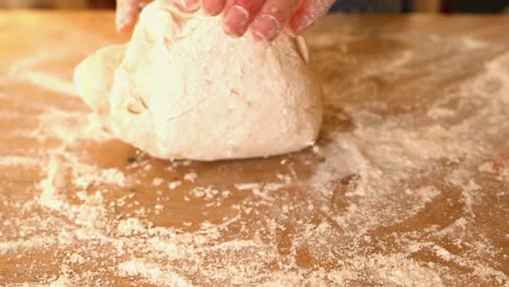 hands kneading ball of dough on a floury surface