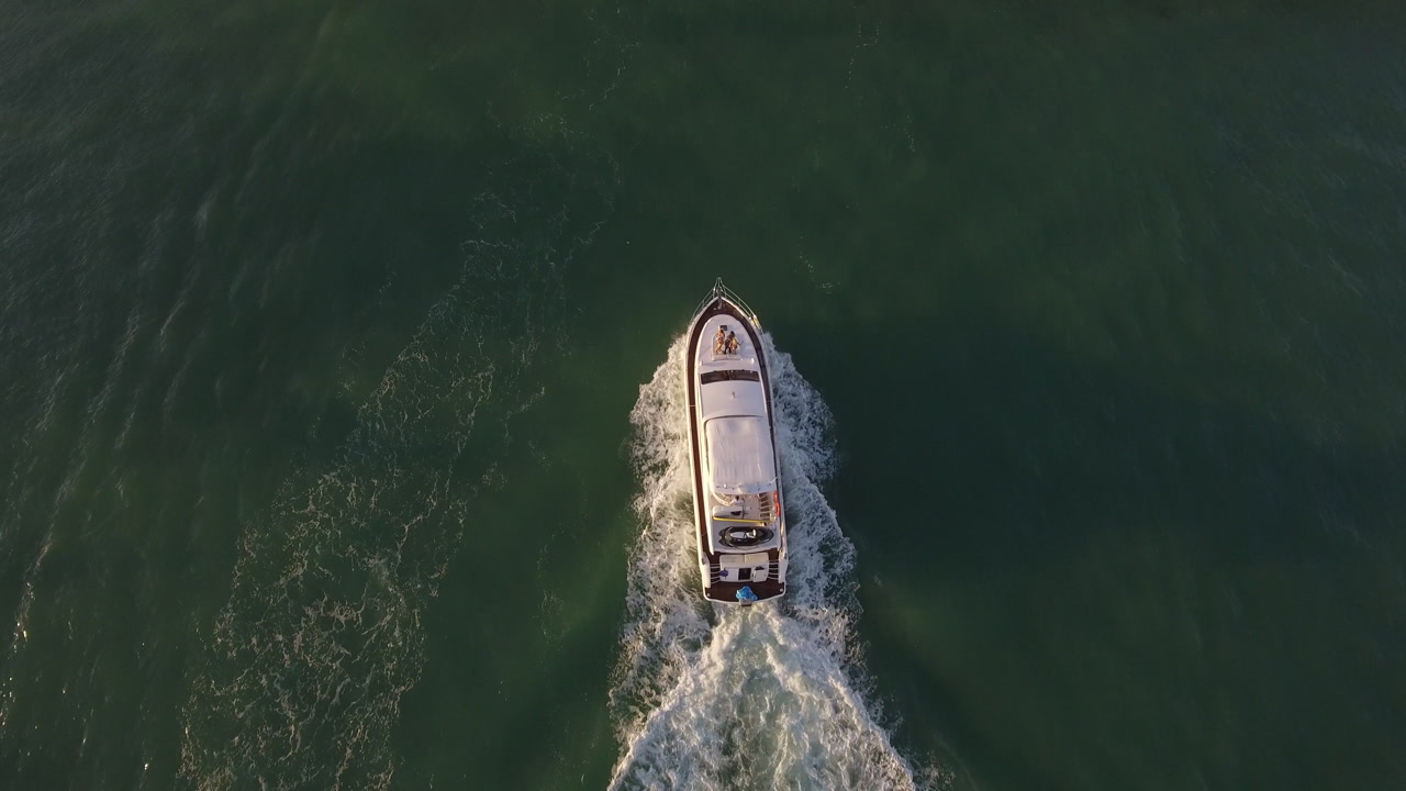 Overhead drone view shows a boat moving through calm water with a clear wake.