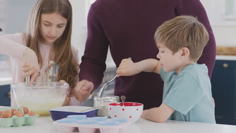 close up of father with two children in kitchen at home having fun baking cakes together