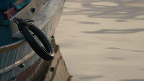 Wooden-fisherman-boat-with-tyre-reflection-on-water-surface-sea-ocean-lake-at-warm-afternoon-light