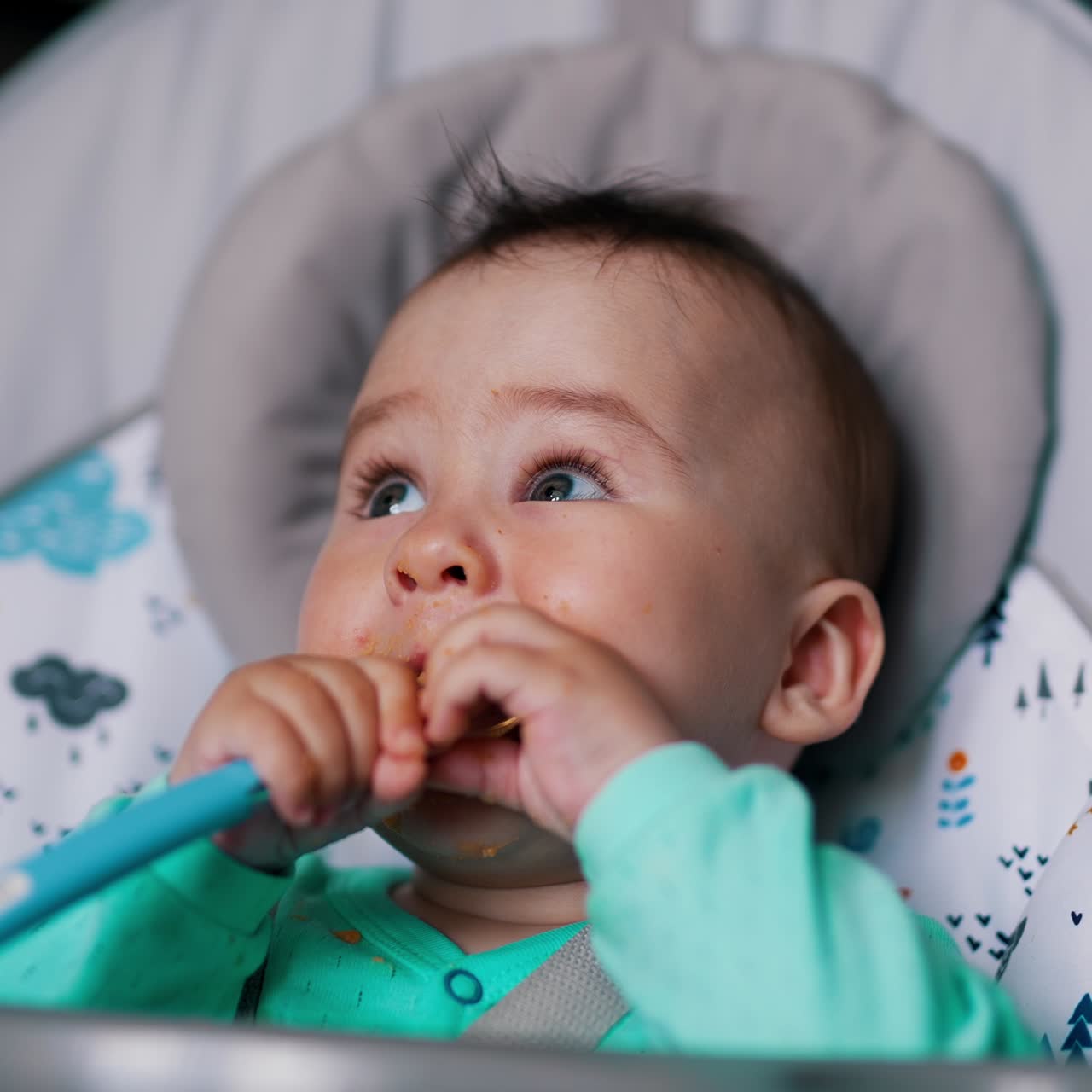 Lovely little boy sitting in a feeding chair. Cute child holds a spoon in his hands and pulls it to his mouth. Close up