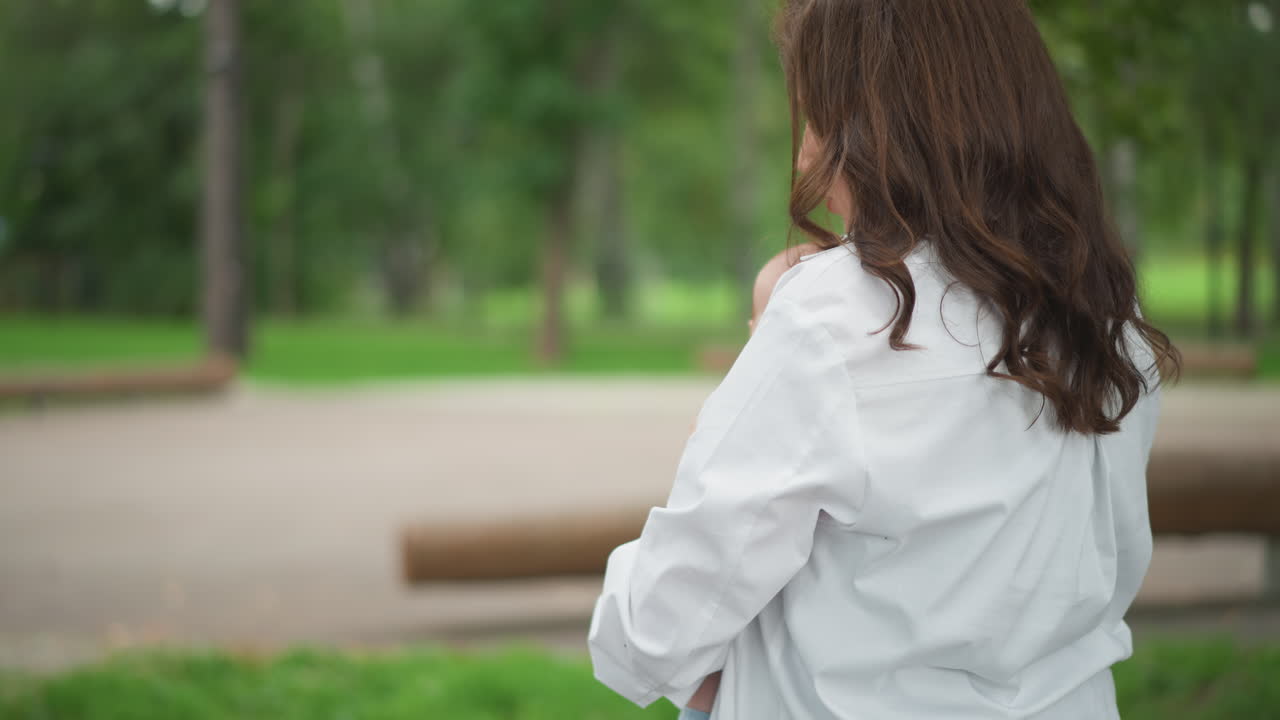 白人母親在公園裡抱著新生兒，特寫鏡頭展現溫柔的親密連結和輕柔的眼神，雙手輕托嬰兒脆弱的頭部，穿著柔軟的白色服飾，寧靜的綠色背景，一個安靜的孕期生活瞬間。