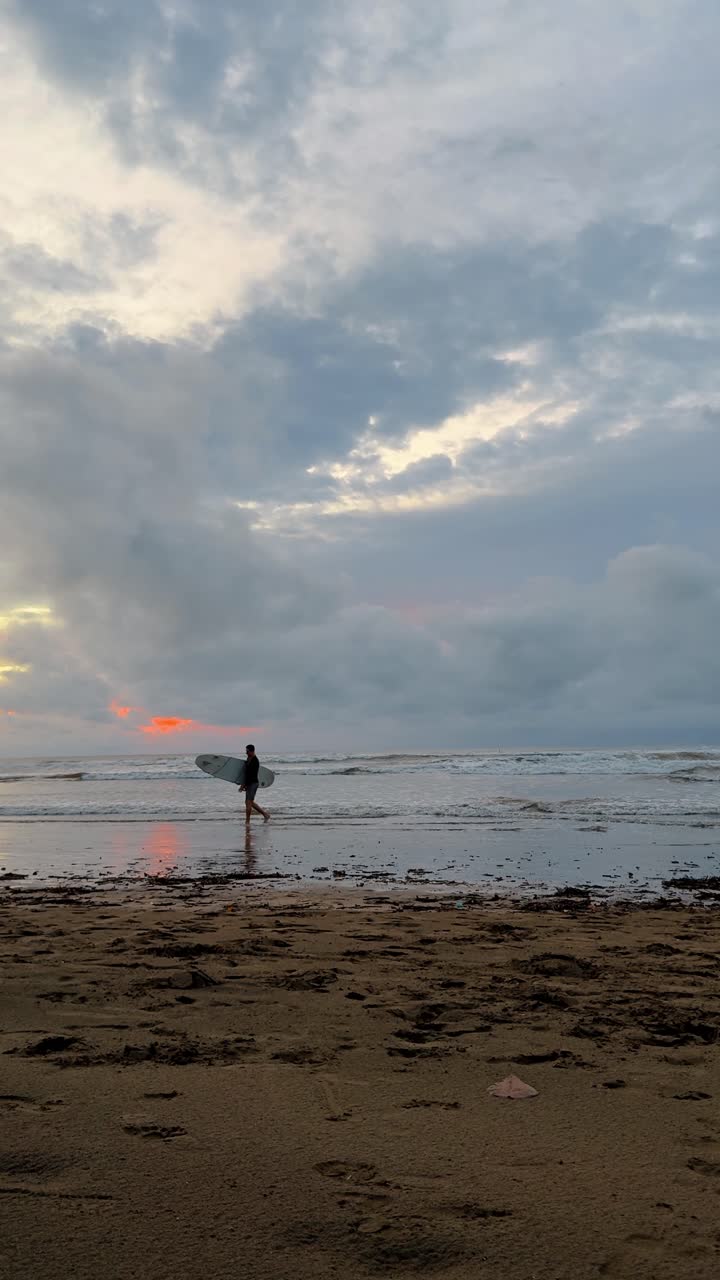 San Jose, Costa Rica, 4. august 2025: Surfer bærer surfbræt på strand under solnedgang i Costa Rica. Silhuet af en mand, der bærer et surfbræt, går på en våd sandstrand i skumringen med orange skyer.