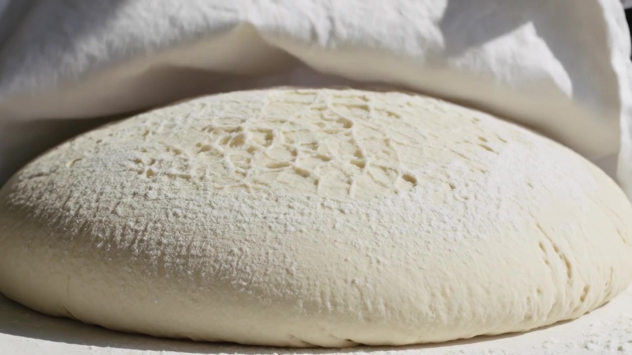 Lifting chef wearing white jacket apron pulling linen cloth from dough on dusty bench checking rise