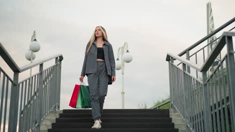 lady carrying shopping bags walking down stairs while glancing at her steps, lamp post visible in the background with iron railings on both sides of the stairs