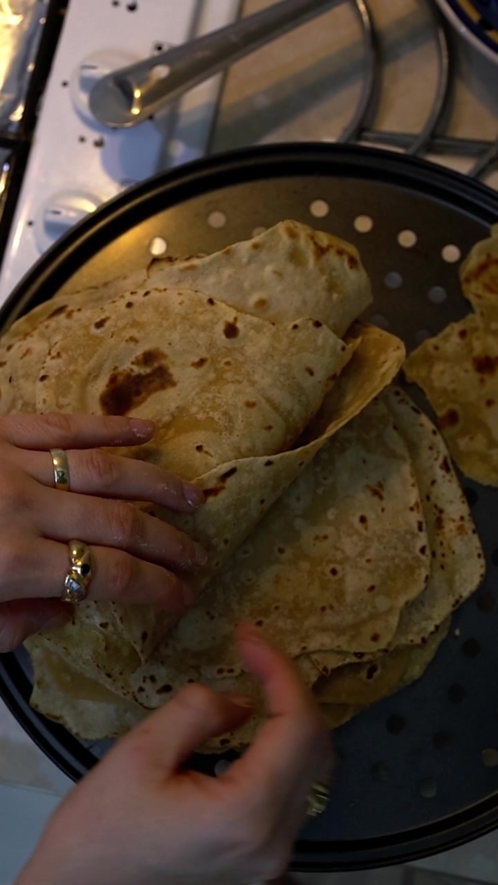 Orang memegang roti pipih chapati hangat yang baru matang dari wajan anti lengket, menampilkan teknik memasak tradisional India dan persiapan roti rumahan