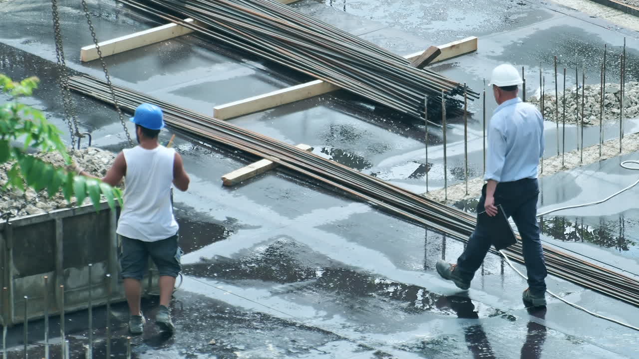 Construction workers walking on a wet concrete foundation at a building site
