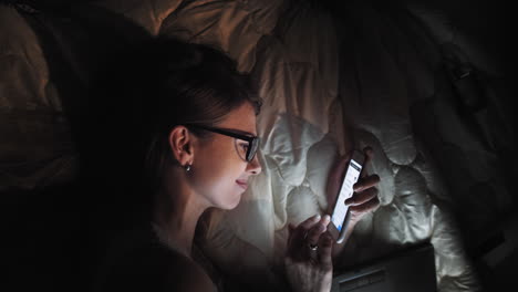 woman using phone in bed at night