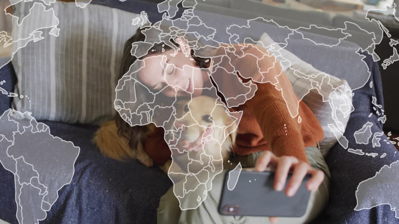 Woman picking up smartphone and framing dog selfie on couch, world map overlay for social media