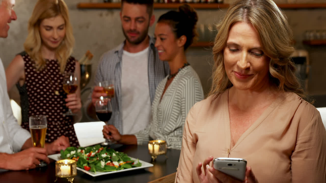 mujer usando su teléfono móvil mientras amigos interactúan en segundo plano 4k 4k