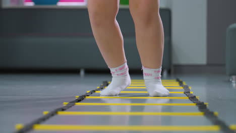 leg view of person jumping on agility ladder for stability and coordination with partial view of couch in background, fitness drill focuses on agility, and endurance training in a gym environment