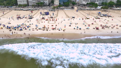 waves run onto white sandy copacabana beach with sunbathers, rio