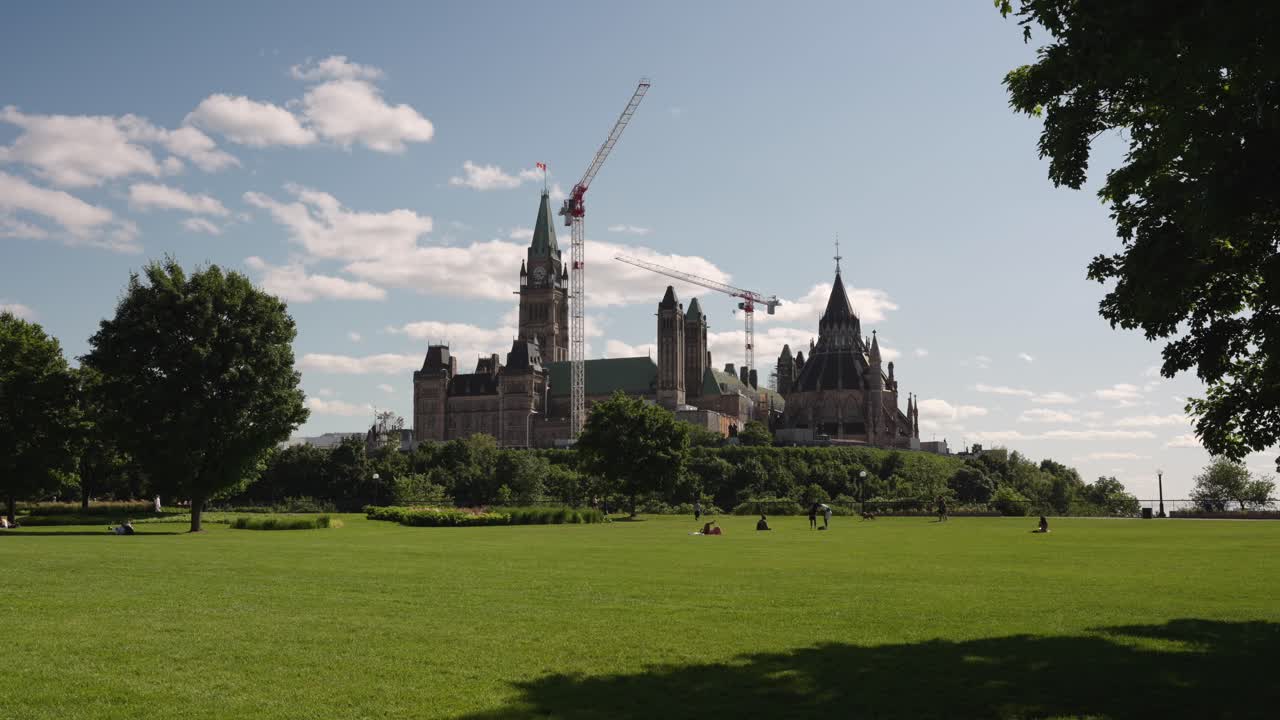 Wide shot of the Parliament of Canada seen from Major's Hill Park in Ottawa, Canada on a sunny summer day with renovation cranes in frame - 4K
