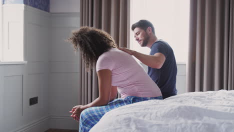 man comforting woman wearing pajamas suffering with depression sitting on bed at home